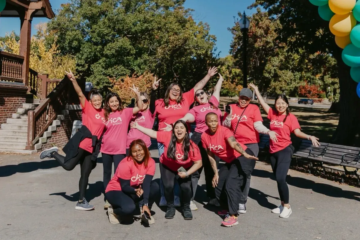 A Chica Project group, all wearing pink, are smiling, waving and celebrating