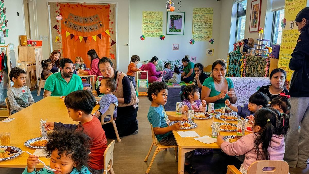 A group of families and little children eat together in a classroom