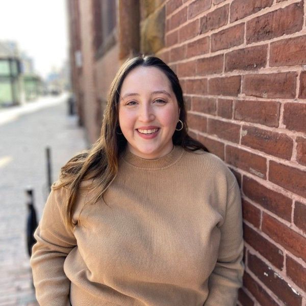 A headshot of a smiling Lorrin Van Evra, leaning on a brick wall