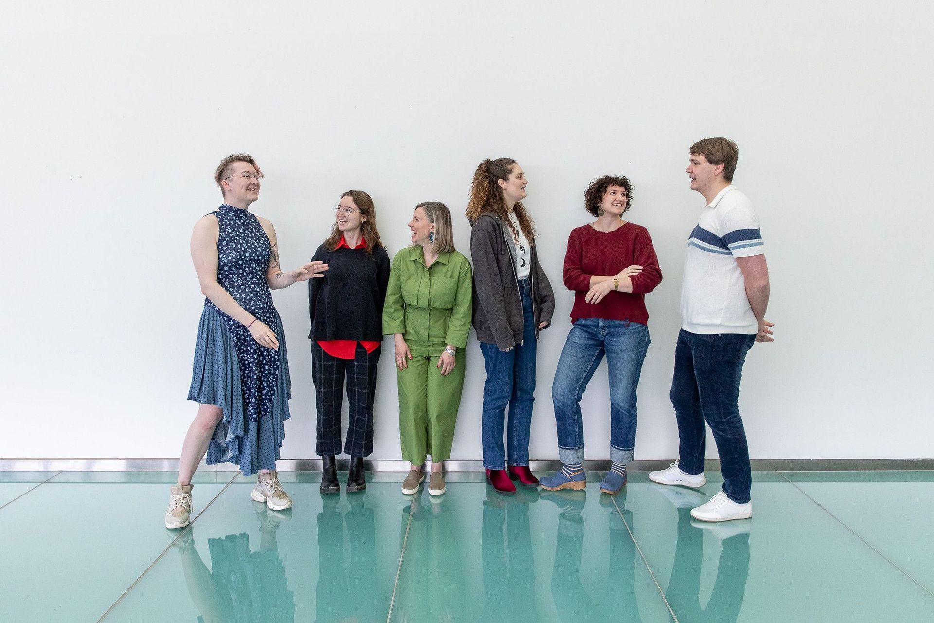 6 members of the realtalk team at CCC. The group is chatting and laughing together standing on a blue glass floor with a white background.