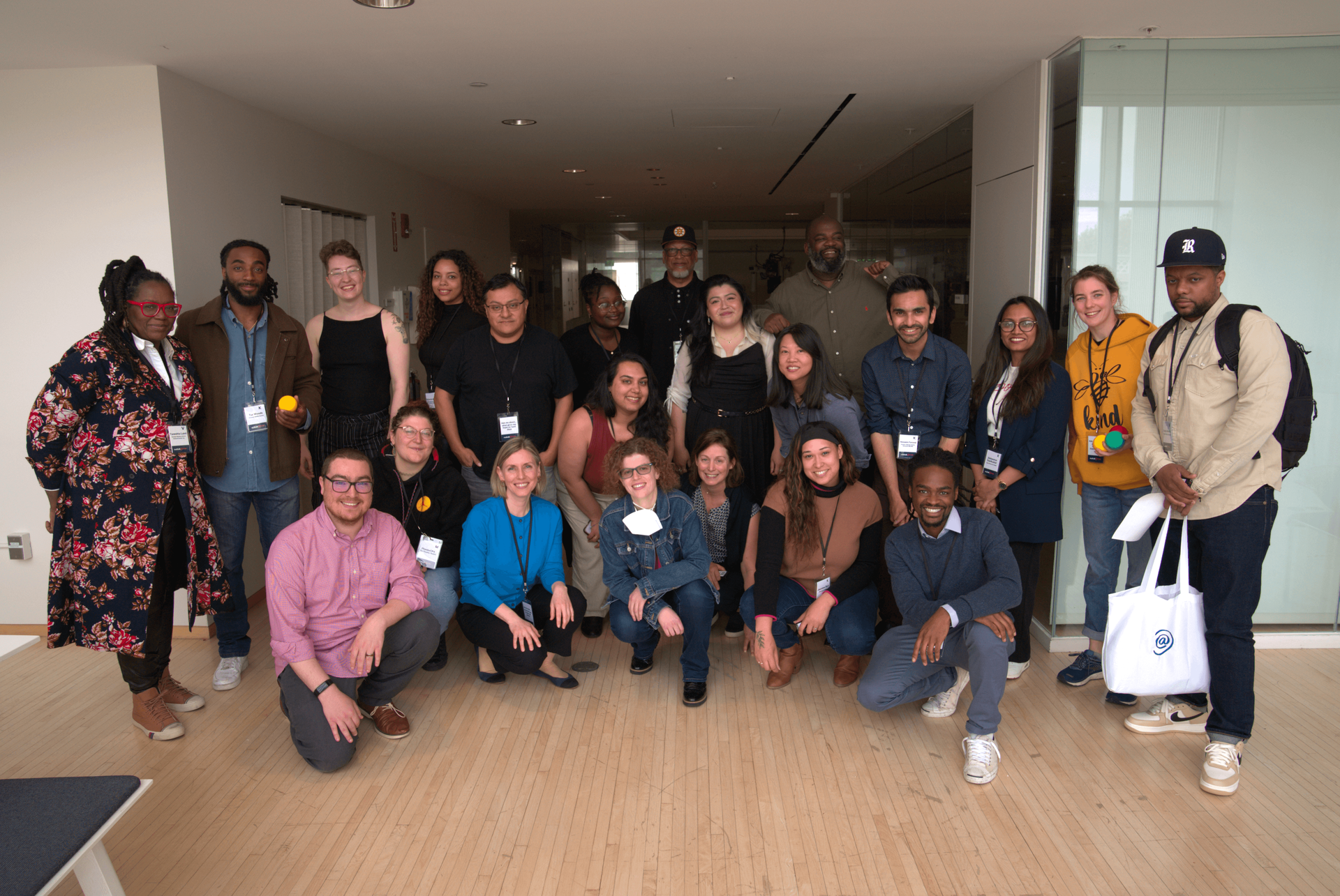 The realtalk@Boston cohort, organizers, and researchers pose together in the MIT Media Lab during training day. 8 people crouch in the front row with 14 people in the back row.