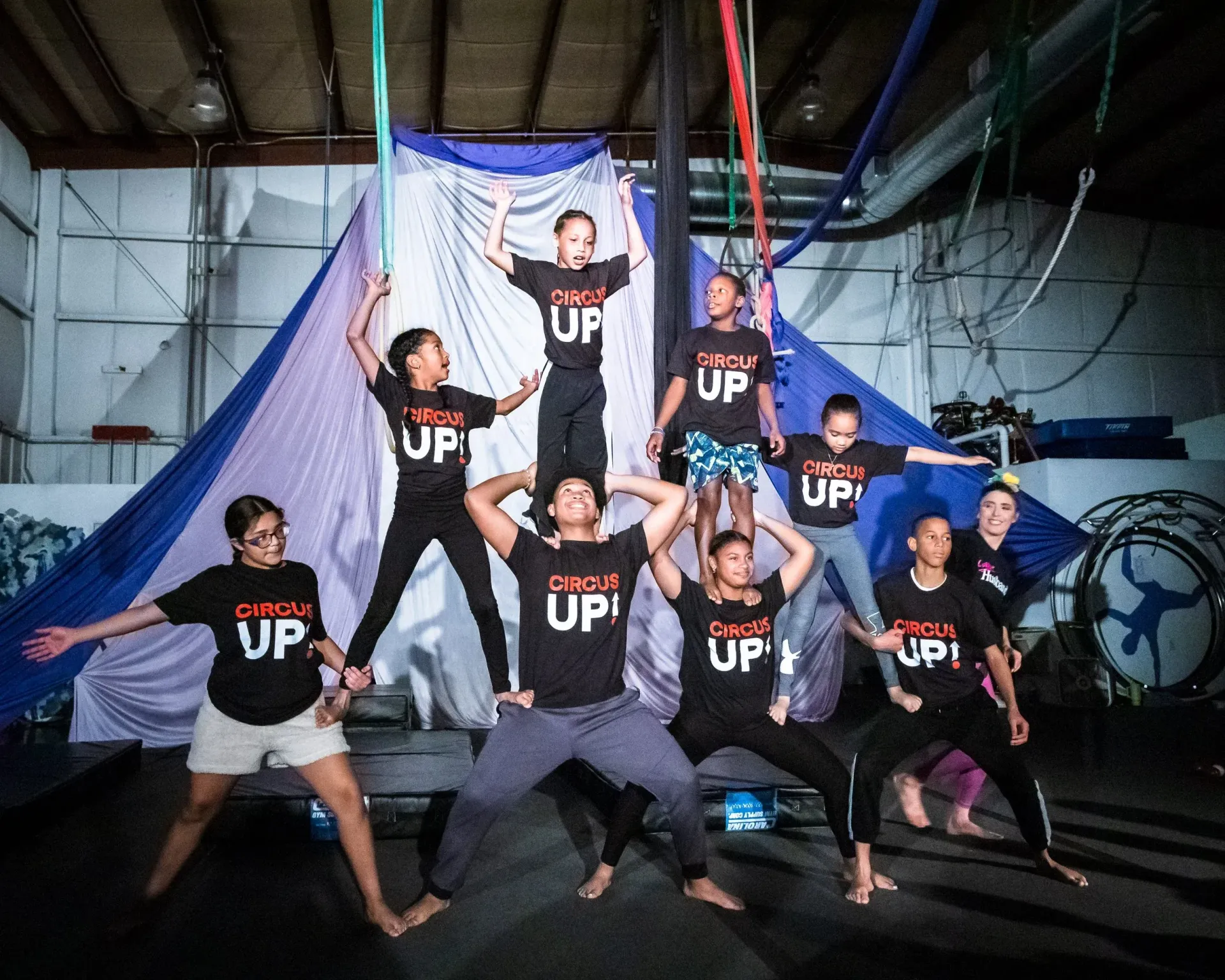 Youth from Circus Up form a human pyramid in front of bright blue silk background